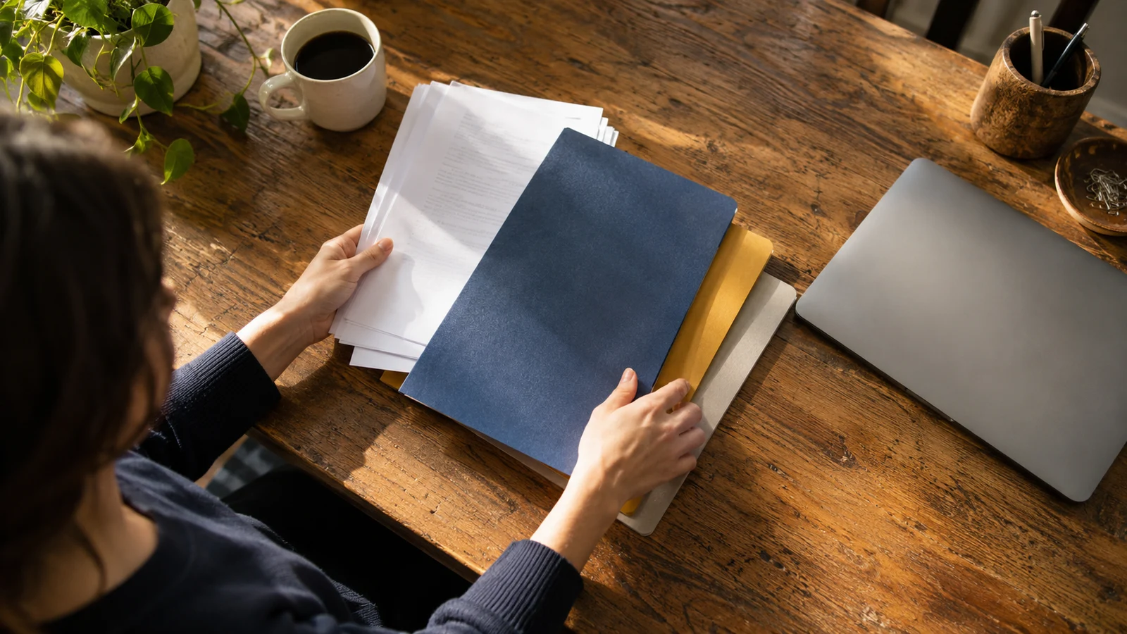 Una persona ordena carpetas y documentos de trabajo sobre una mesa.