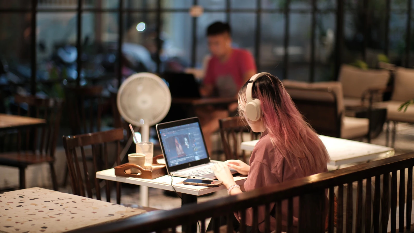Una mujer con auriculares trabaja en la edición de vídeo con un portátil en una cafetería.