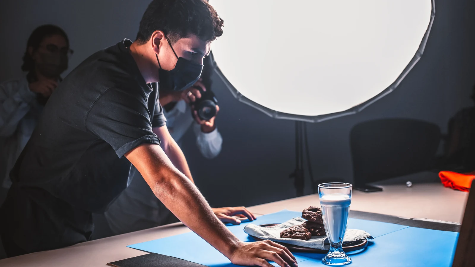 Un equipo prepara una fotografía de producto con un vaso, galletas, cámara e iluminación de estudio.