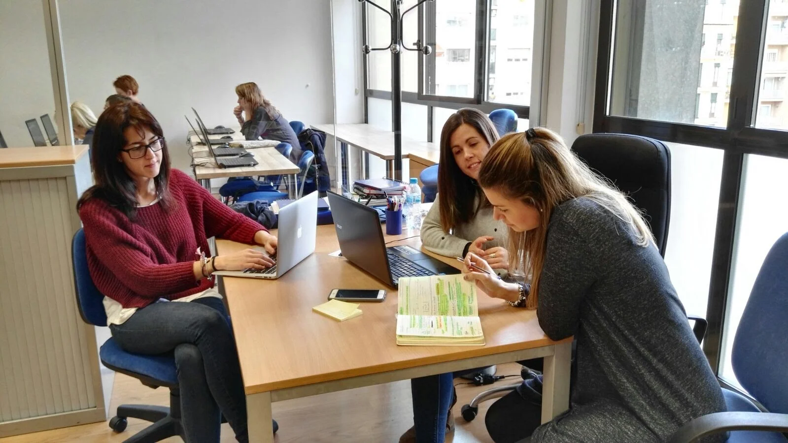 Tres profesionales trabajan alrededor de una mesa en una oficina luminosa.