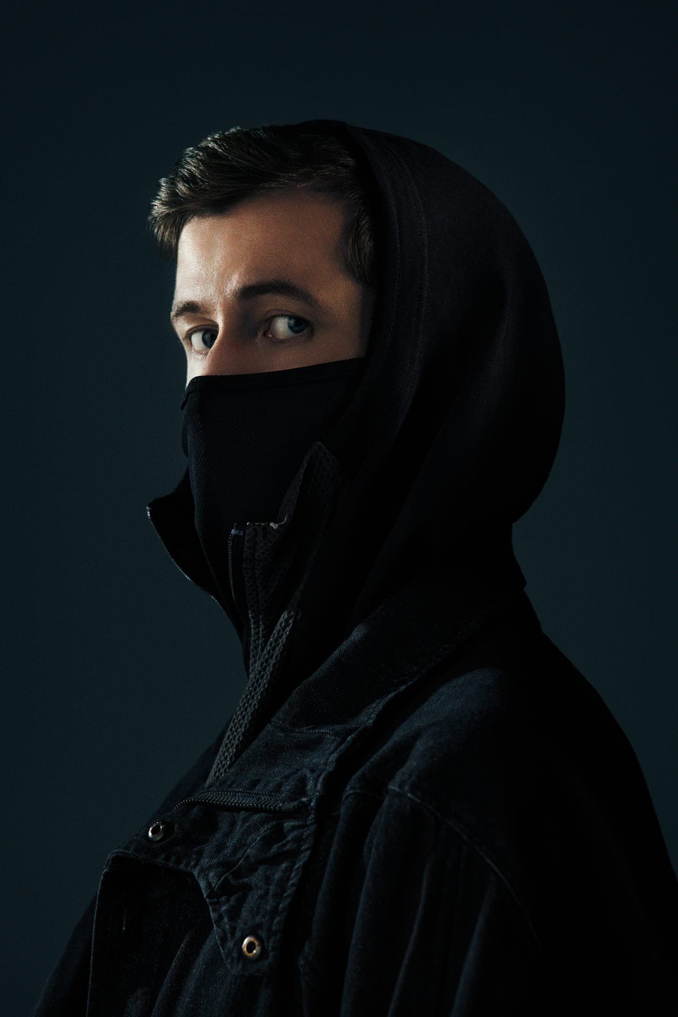 Alan Walker con capucha y mascarilla negras sobre fondo oscuro.