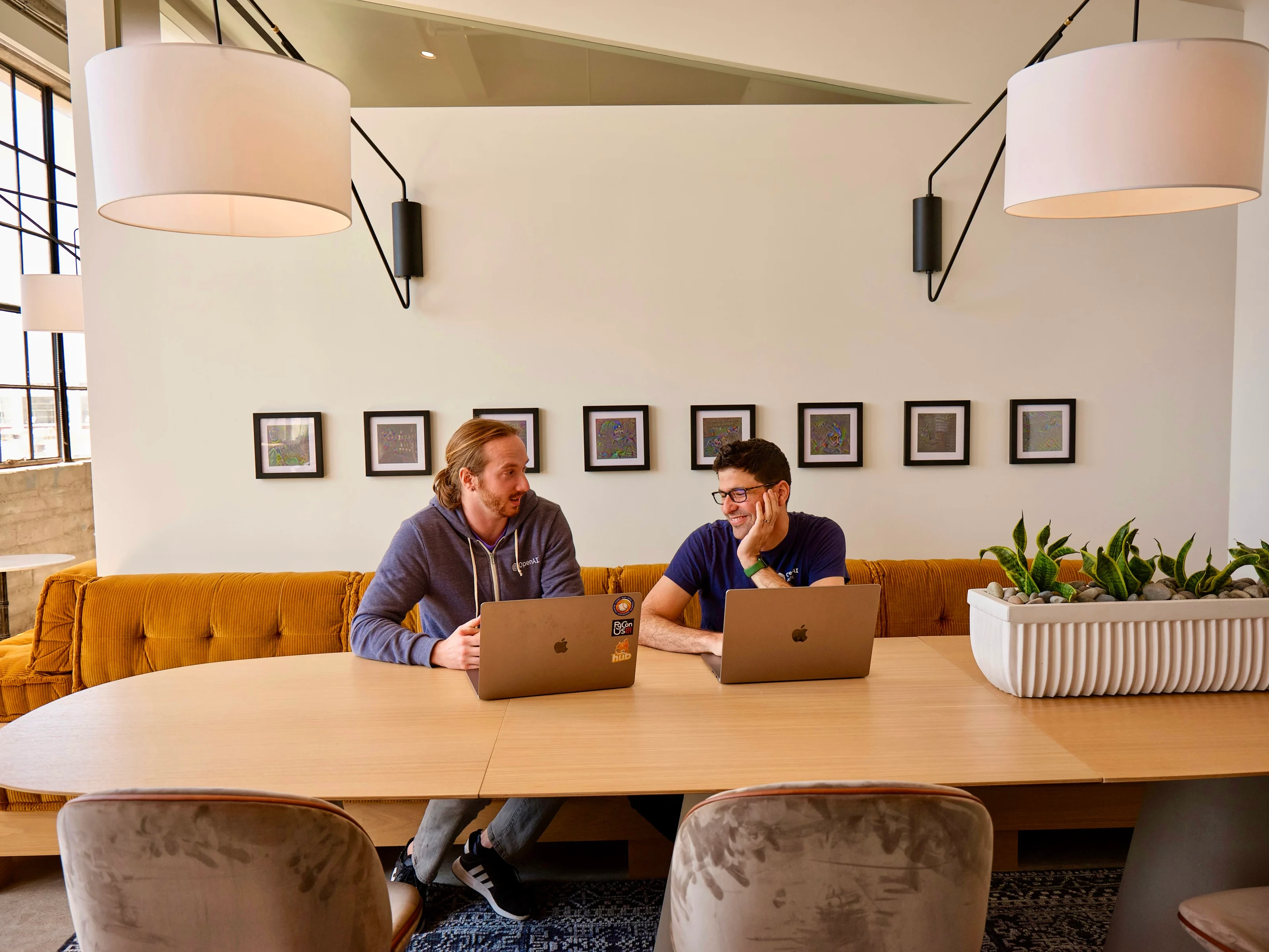 Dos personas trabajando con portátiles en una mesa de las oficinas de OpenAI.