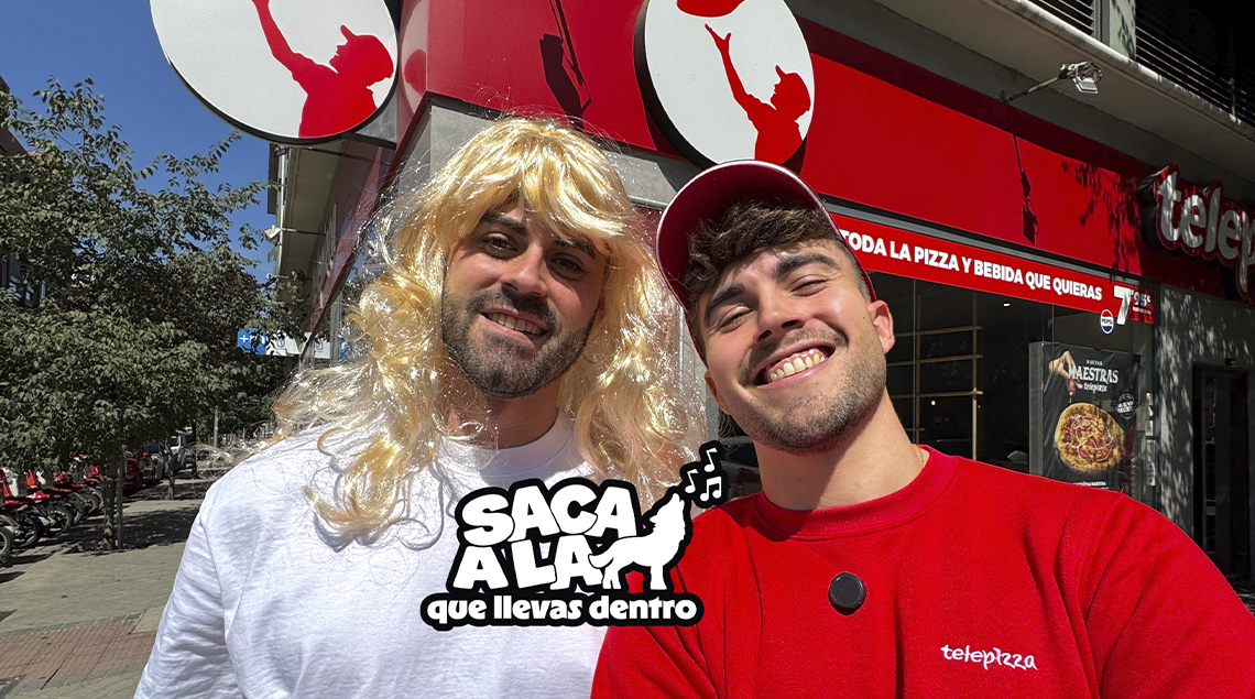 Dos protagonistas de la acción de Telepizza posan delante de un establecimiento.