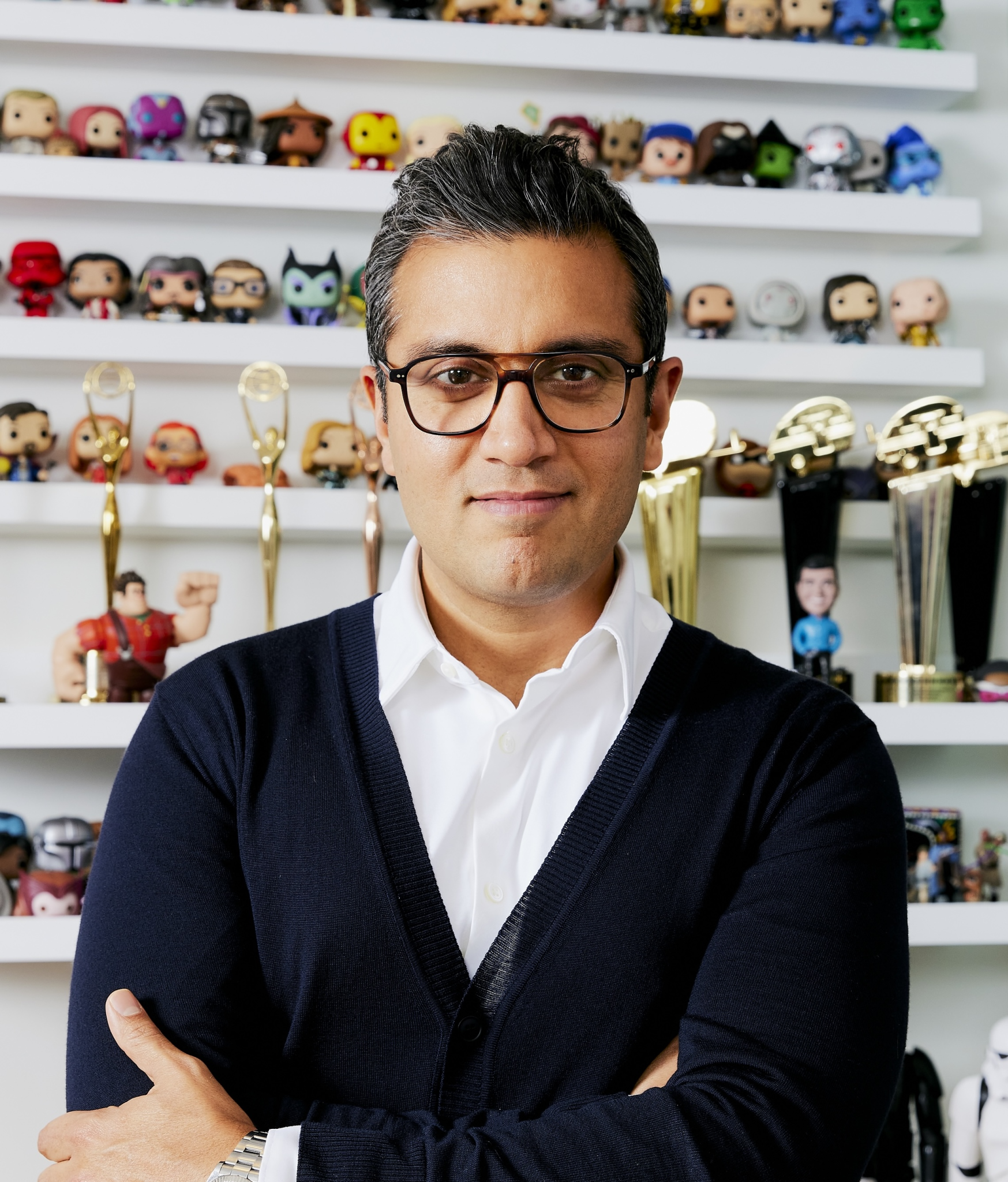 Asad Ayaz posa con los brazos cruzados ante una estantería de figuras y premios.
