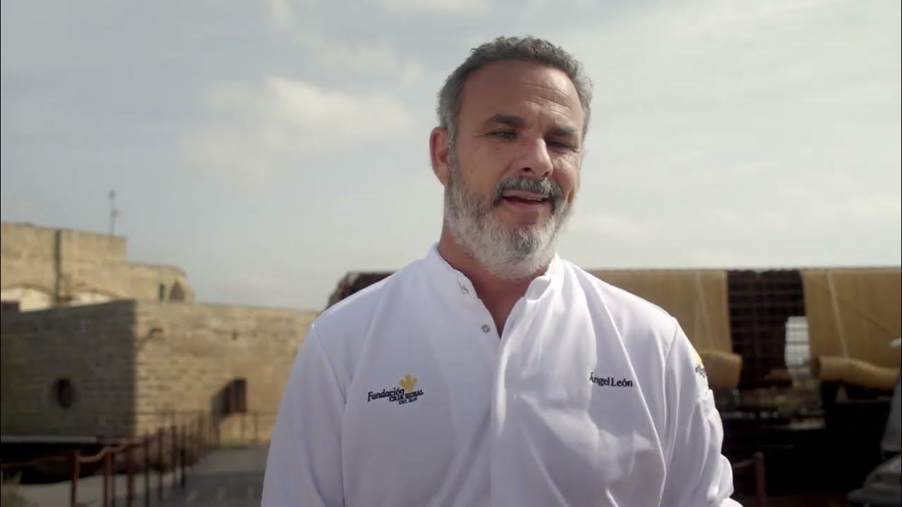 Ángel León con chaquetilla blanca de cocina, al aire libre junto a un edificio de piedra.