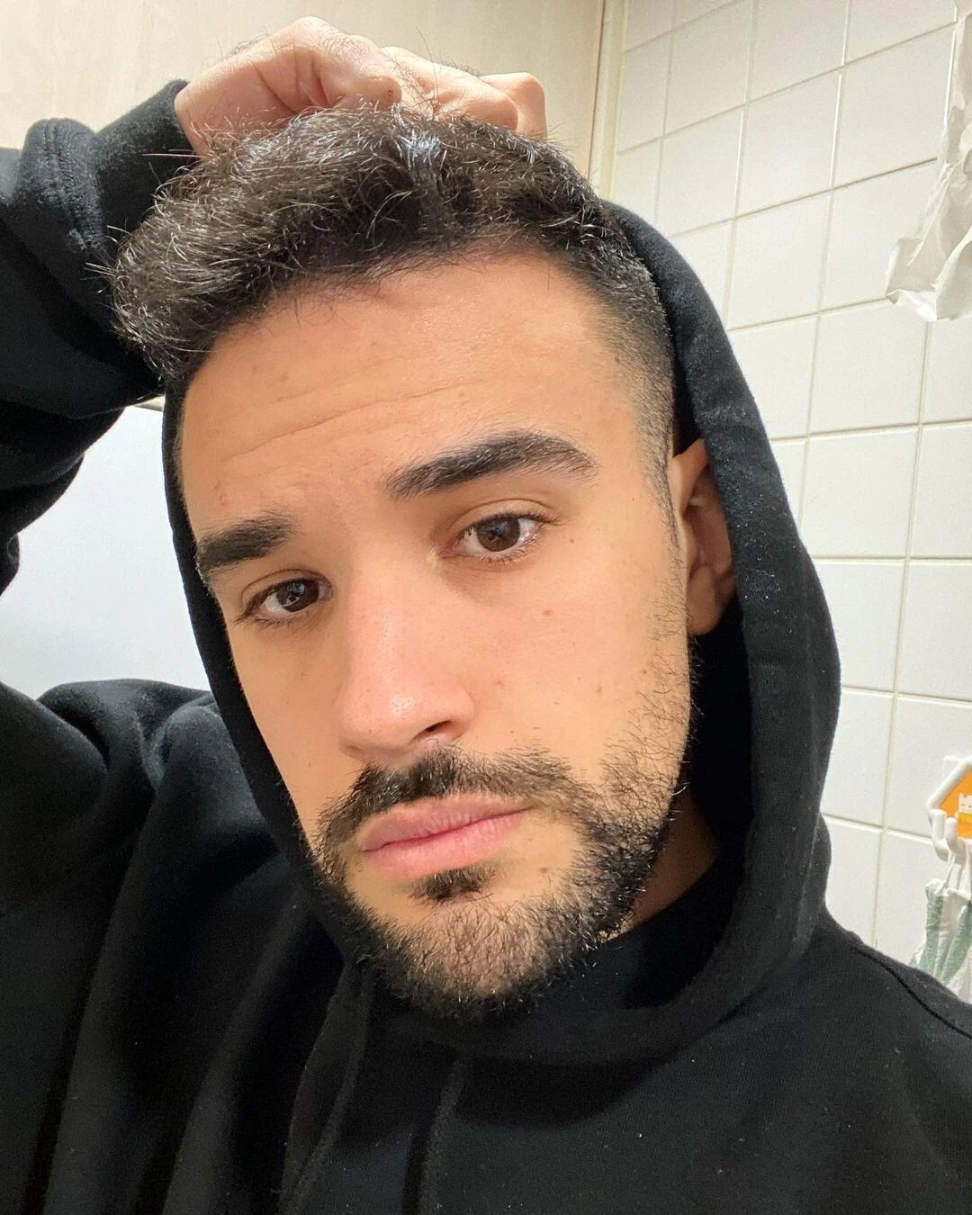 IlloJuan con sudadera negra sujetándose la capucha.